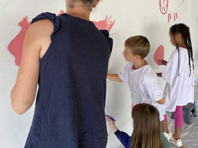 Peindre avec les enfants au cours d'une médiation artistique pour une fresque réalisée sur un mur d'un accueil de loisirs